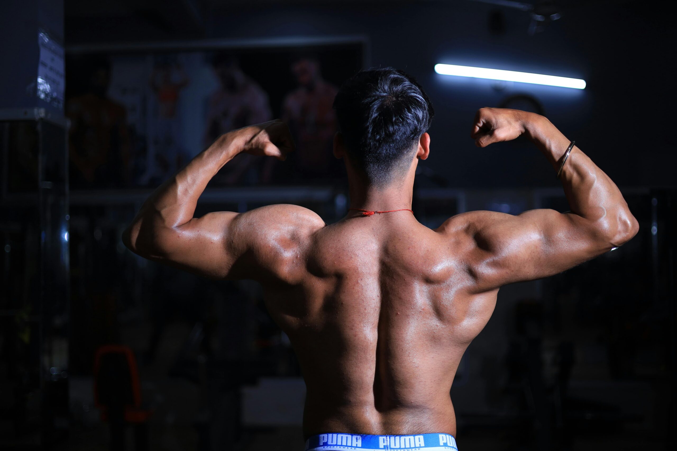 A muscular man flexes his back muscles in a dimly lit gym, showcasing strength and fitness.