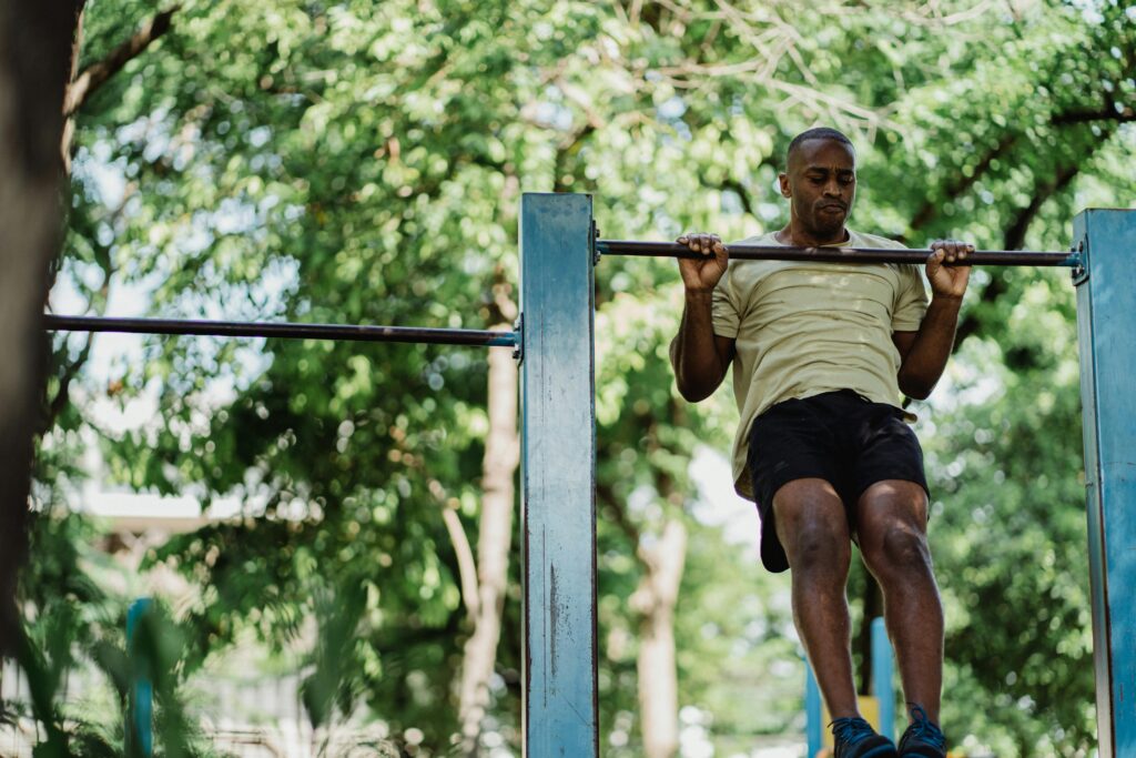 pexels-photo-4803667-4803667 An athletic adult man doing a pull-up on an outdoor metal bar surrounded by green trees.