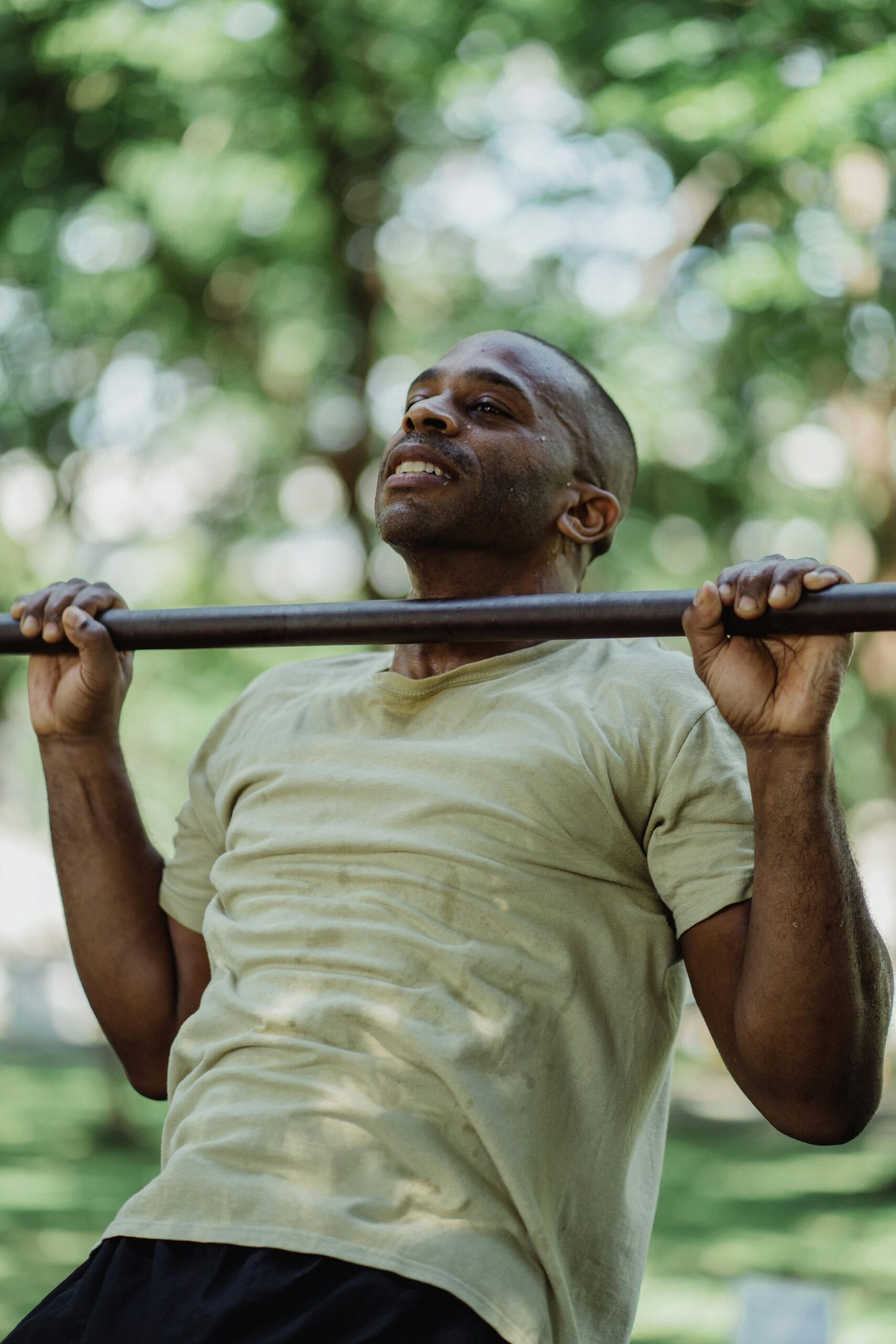 A strong man performing pull-ups on a bar outdoors, showcasing fitness and strength.