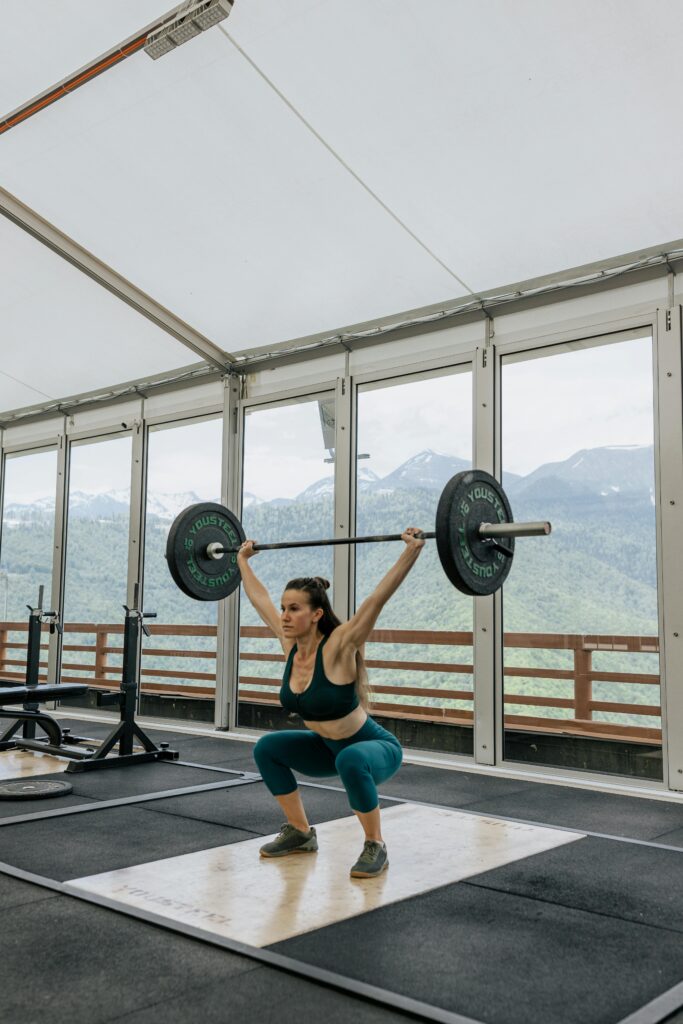 pexels-photo-4943914-4943914 Adult woman lifting weights with mountains visible through gym windows.