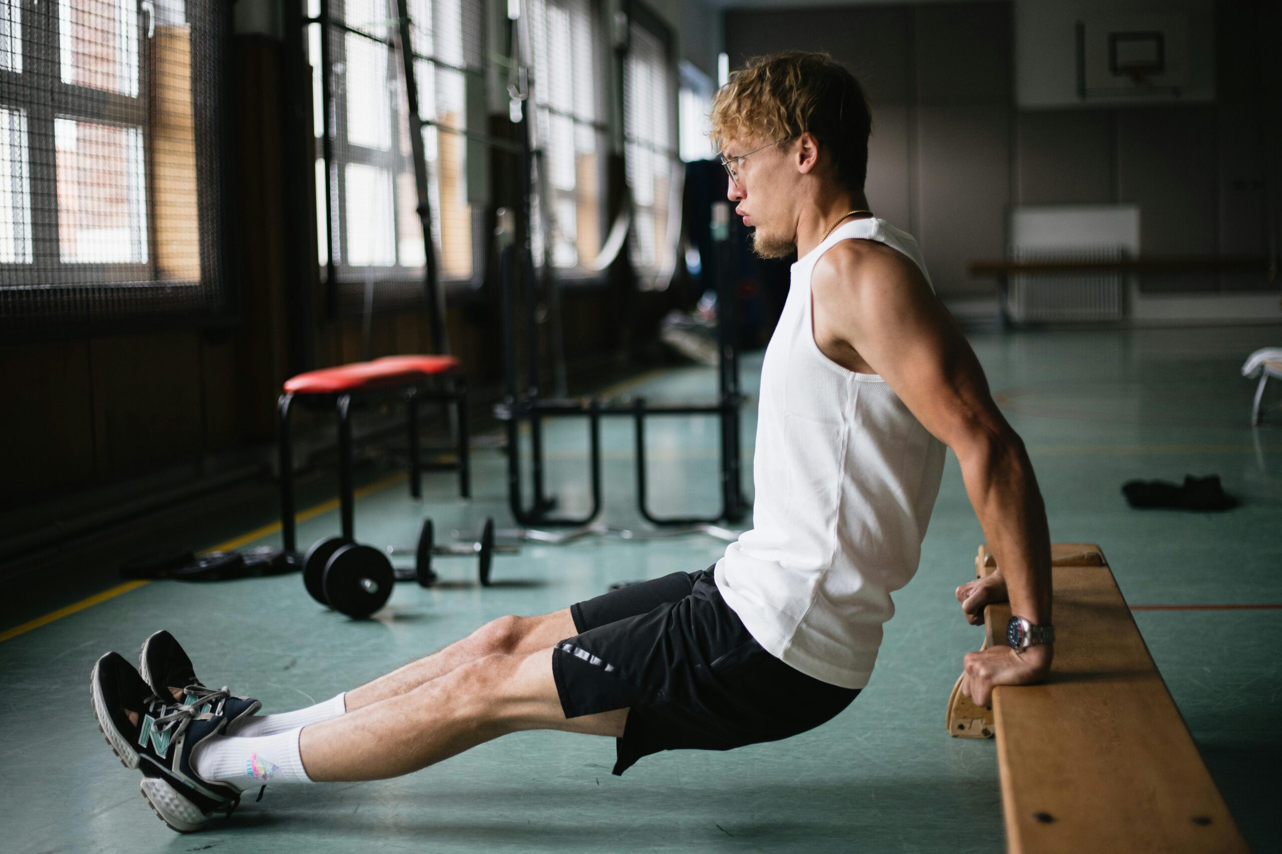 A young man performing a tricep dip exercise in a well-lit gym setting.