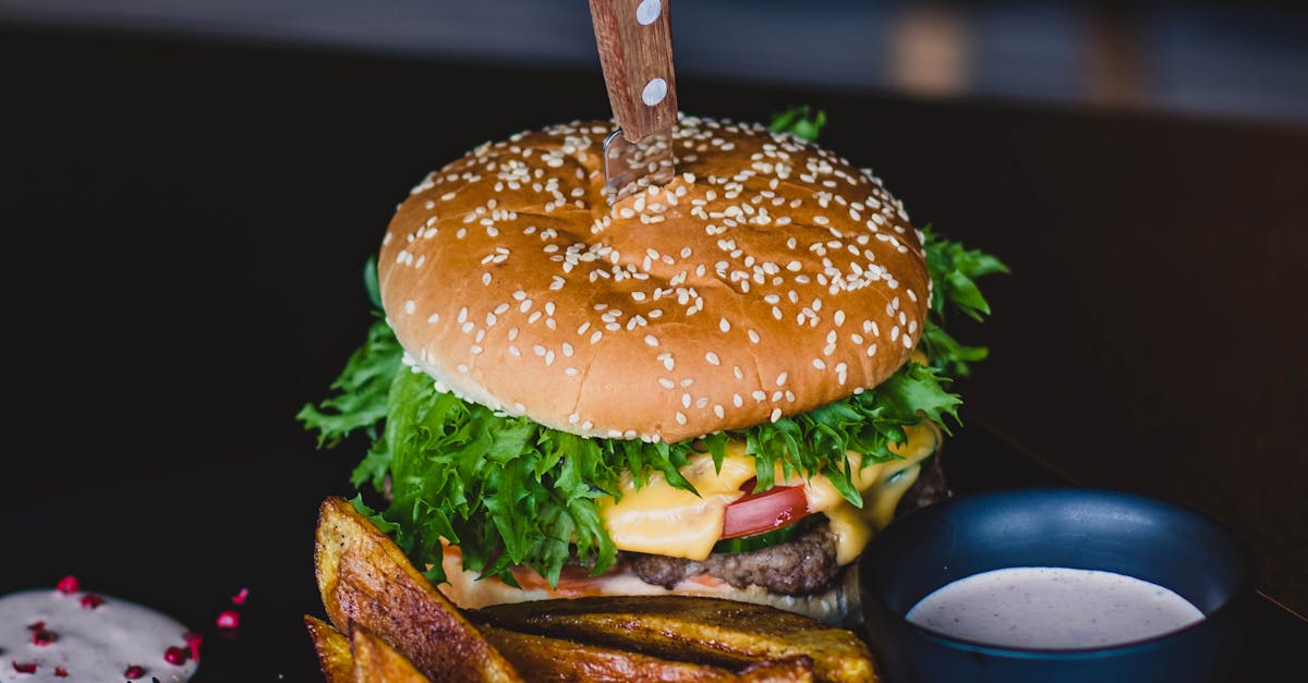 Close-up of a gourmet cheeseburger with wedges and tomato on a black plate.