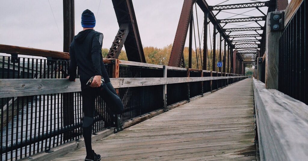 Man stretching on a wooden footbridge during a daytime run on an iron bridge, emphasizing fitness and recreation.