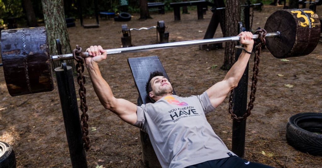 Man weightlifting outdoors, using a bench press setup amid trees for strength training.