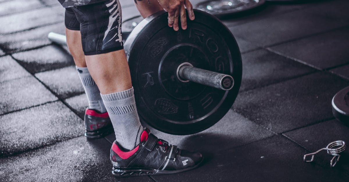 A focused man lifting a heavy barbell during weightlifting exercise in a gym. mollets