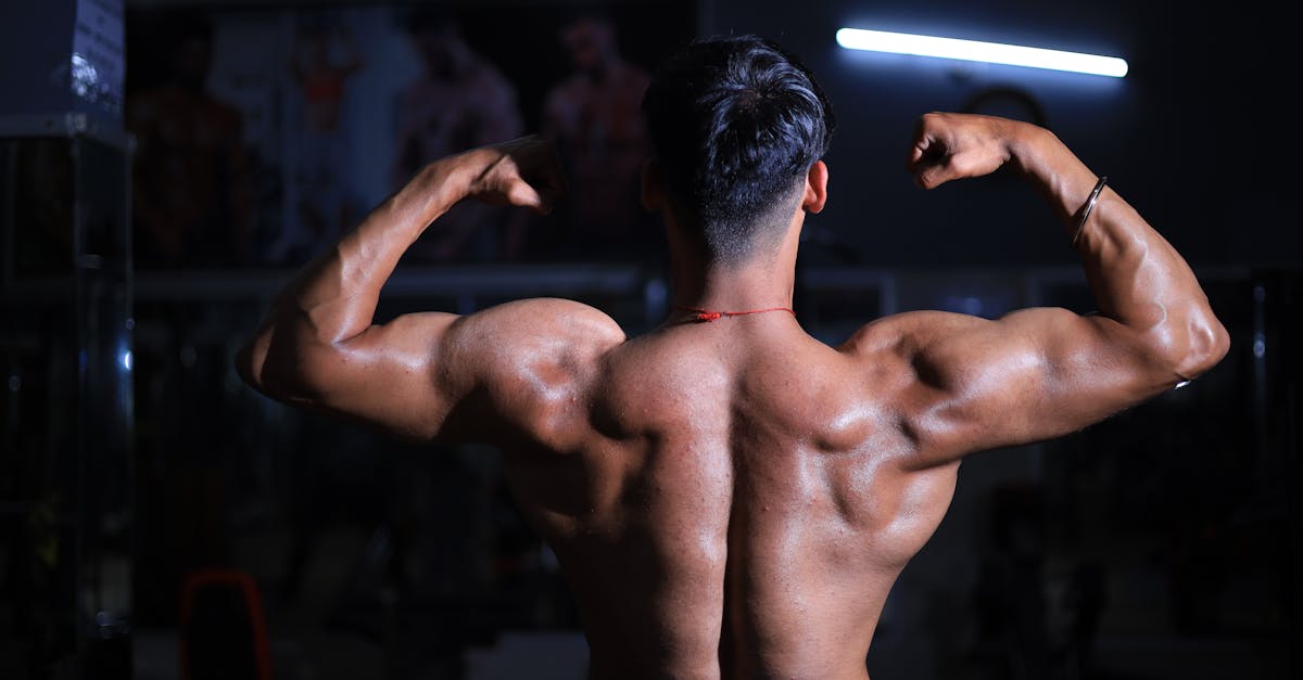 A muscular man flexes his back muscles in a dimly lit gym, showcasing strength and fitness.