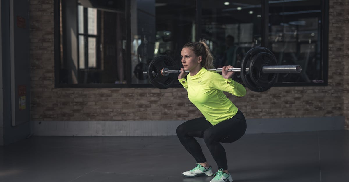 Dedicated woman in neon activewear performs a weighted squat in an indoor gym setting.