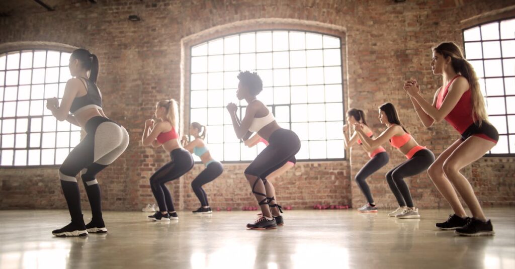 Women participating in a group fitness class performing squats in an industrial-style studio. Femmes travaillant leurs fessiers.
