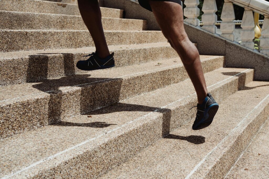 Close-up of a runner's legs ascending stone steps, capturing movement and shadow play. Travail des mollets.