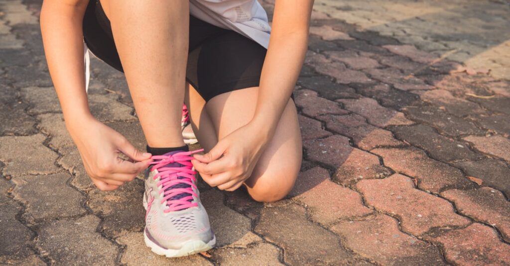 Adult woman tying pink laces on running shoes outdoors. Focuses on fitness and lifestyle.