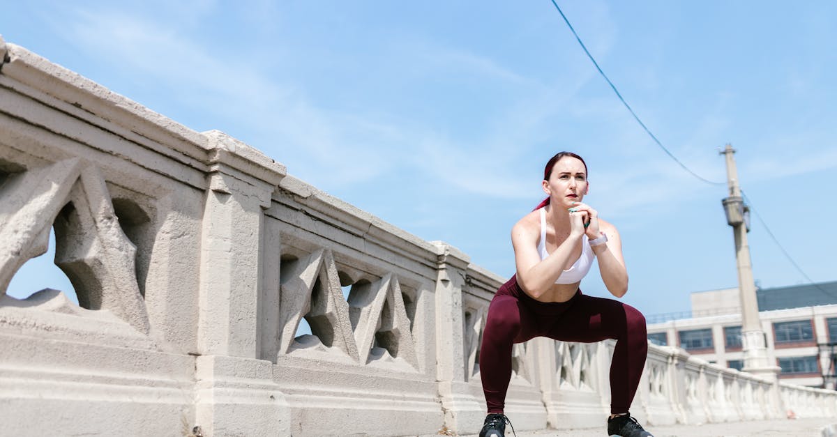 Woman performing a squat exercise outdoors beside a concrete railing under a clear sky.