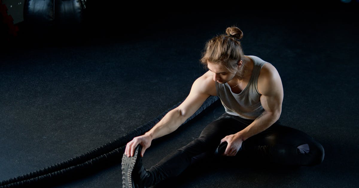 Muscular male athlete stretching on gym floor with battle ropes.