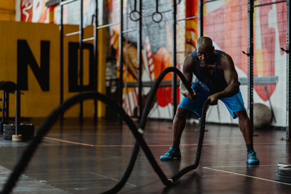 A muscular man doing HIIT exercises with battle ropes in an indoor gym setting, showcasing strength and fitness.