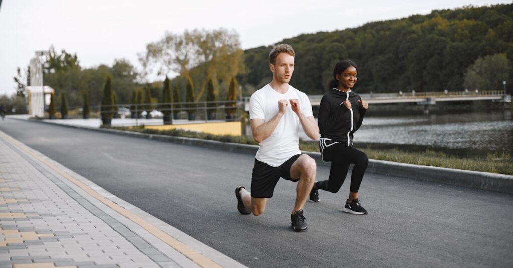A fit couple exercises by a scenic riverside, performing lunges in activewear, showcasing outdoor fitness.