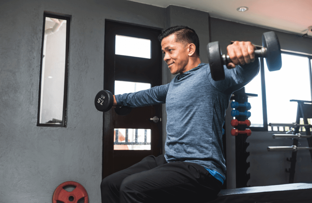 Jeune homme exécutant des élévations latérales aux haltères assis dans une salle de sport.