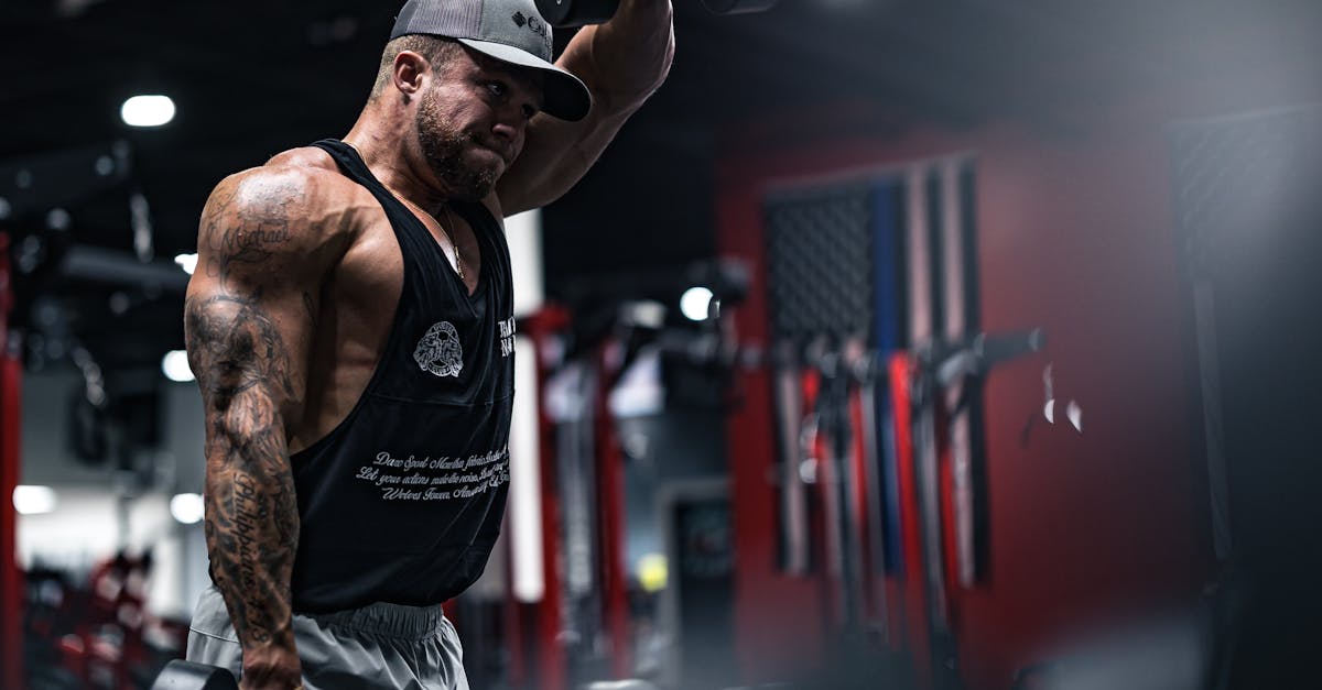 Un homme musclé fait des exercices d'élévation frontales avec des haltères dans un environnement de salle de sport moderne.